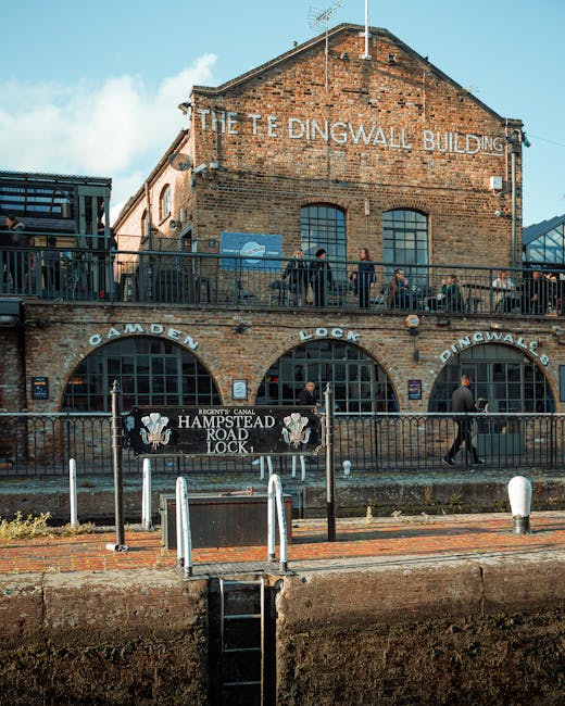 The exterior of the historic Dingwall Building in Hampstead, constructed from red bricks and featuring large arched windows on the ground floor, which are partly obscured by a black metal fence. A sig